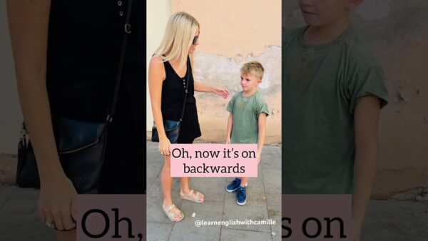 A person in a black dress talks to a child in a green shirt against a textured wall. Text overlay reads, "Oh, now it’s on backwards."