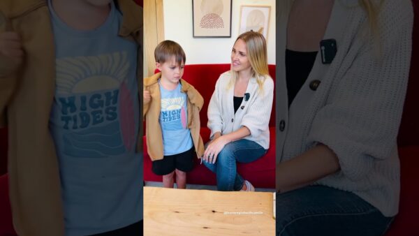 A person and a child sit on a red couch. The child wears a "High Tides" shirt. Framed art hangs on the wall.