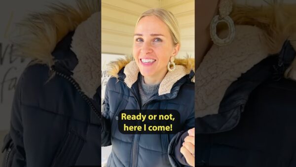 A person in a warm jacket smiles with text overlay: "Ready or not, here I come!" Indoors, with neutral background.