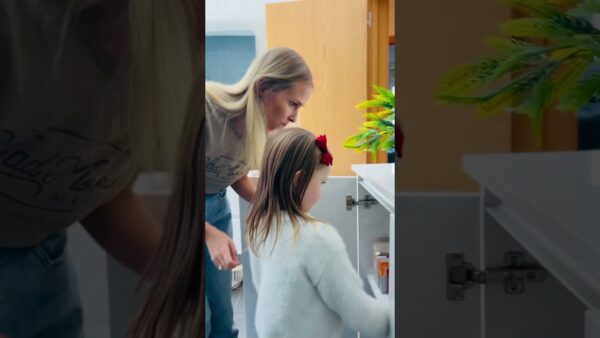 A person and child are looking inside a white cabinet, with a small plant visible on top, in a brightly lit room.