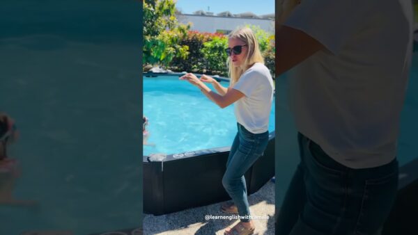 A person stands by a pool, gesturing playfully. They're wearing sunglasses, a white shirt, and jeans. Lush greenery is in the background.